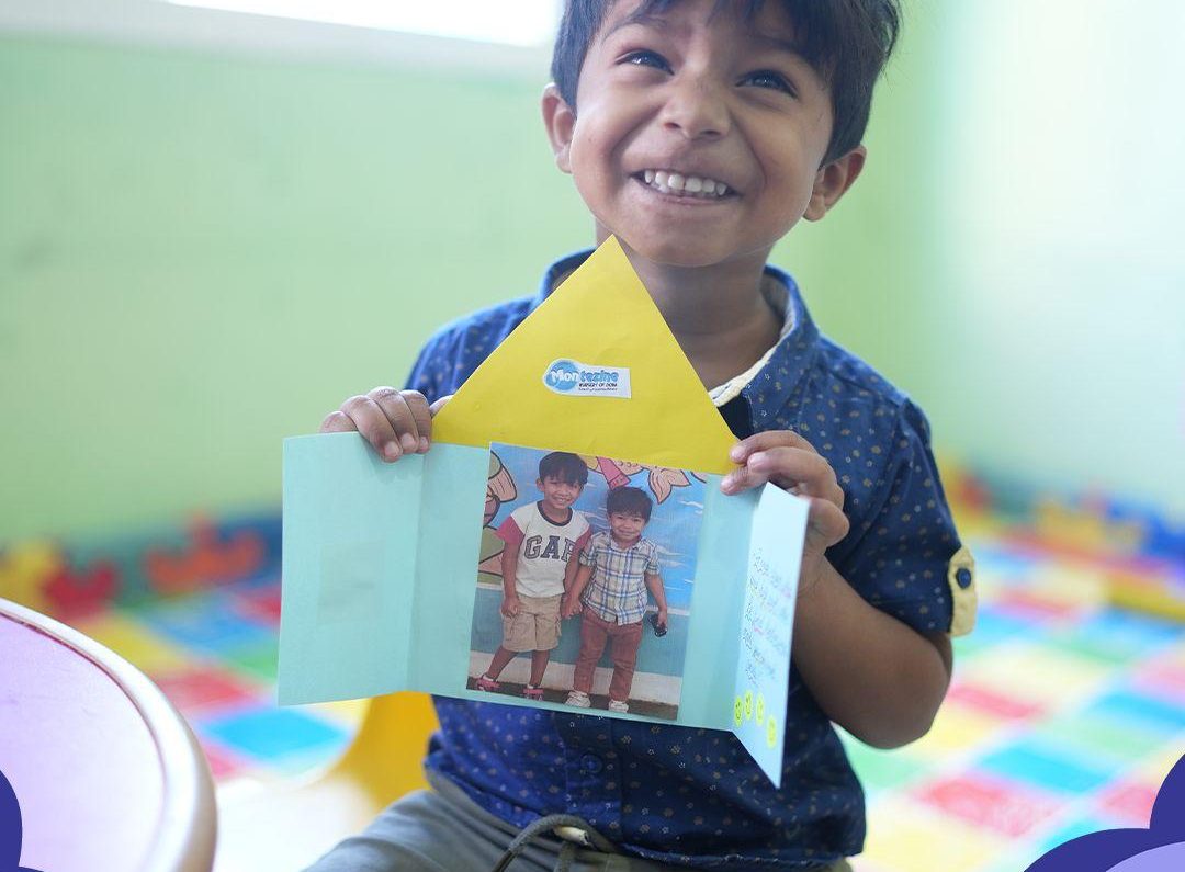 A boy at Montezine Nursery beaming while holding up a card he made in class