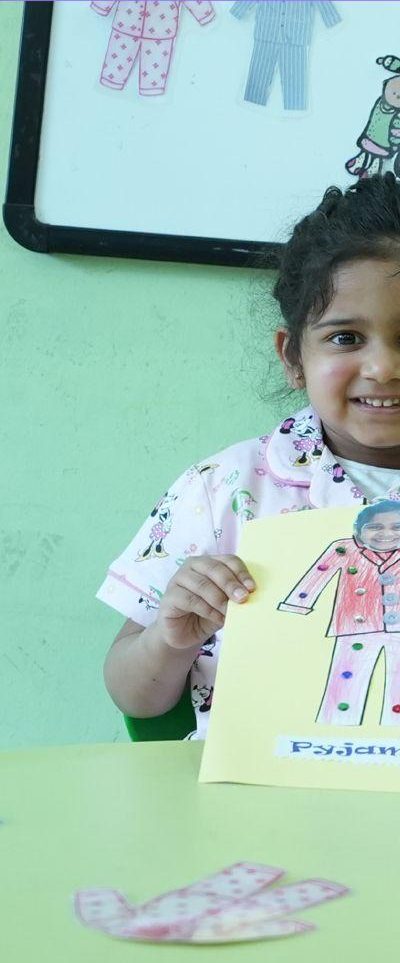 A young girl smiling while holding up a pajama-themed craft she made